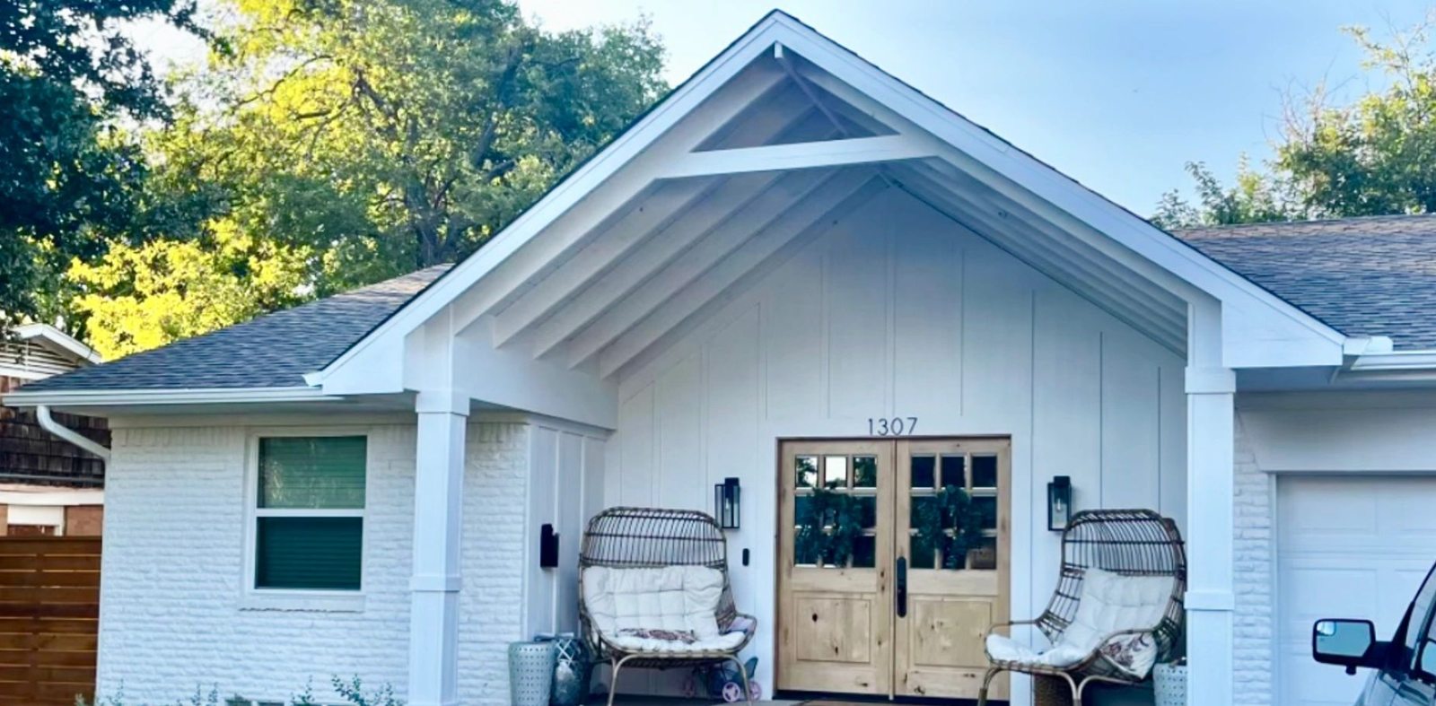 Renovated white farmhouse exterior with gabled cedar porch